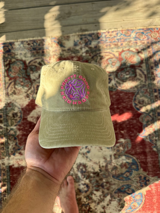 Khaki cap with a purple logo held by a hand on a patterned rug