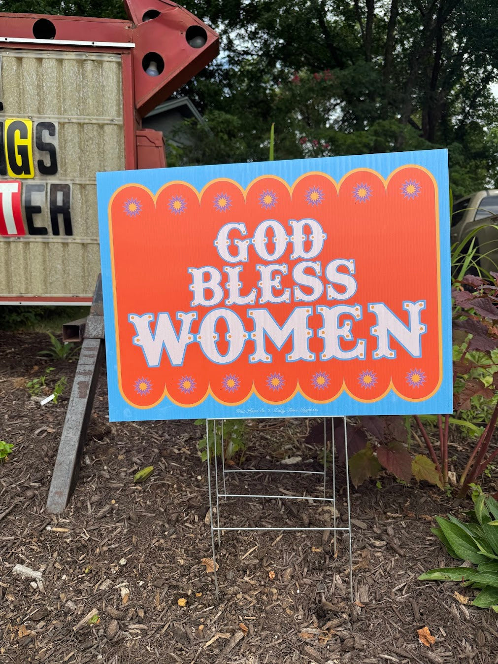 Outdoor sign with 'GOD BLESS WOMEN' text in a decorative frame.